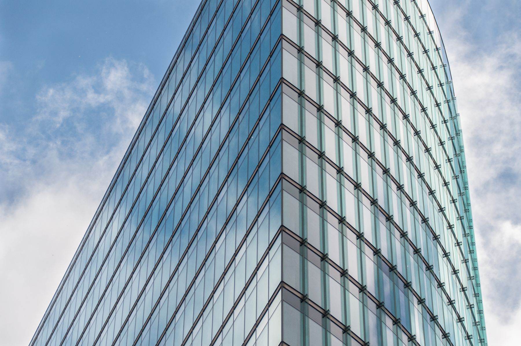 Looking up at a curved glass office tower against a blue sky