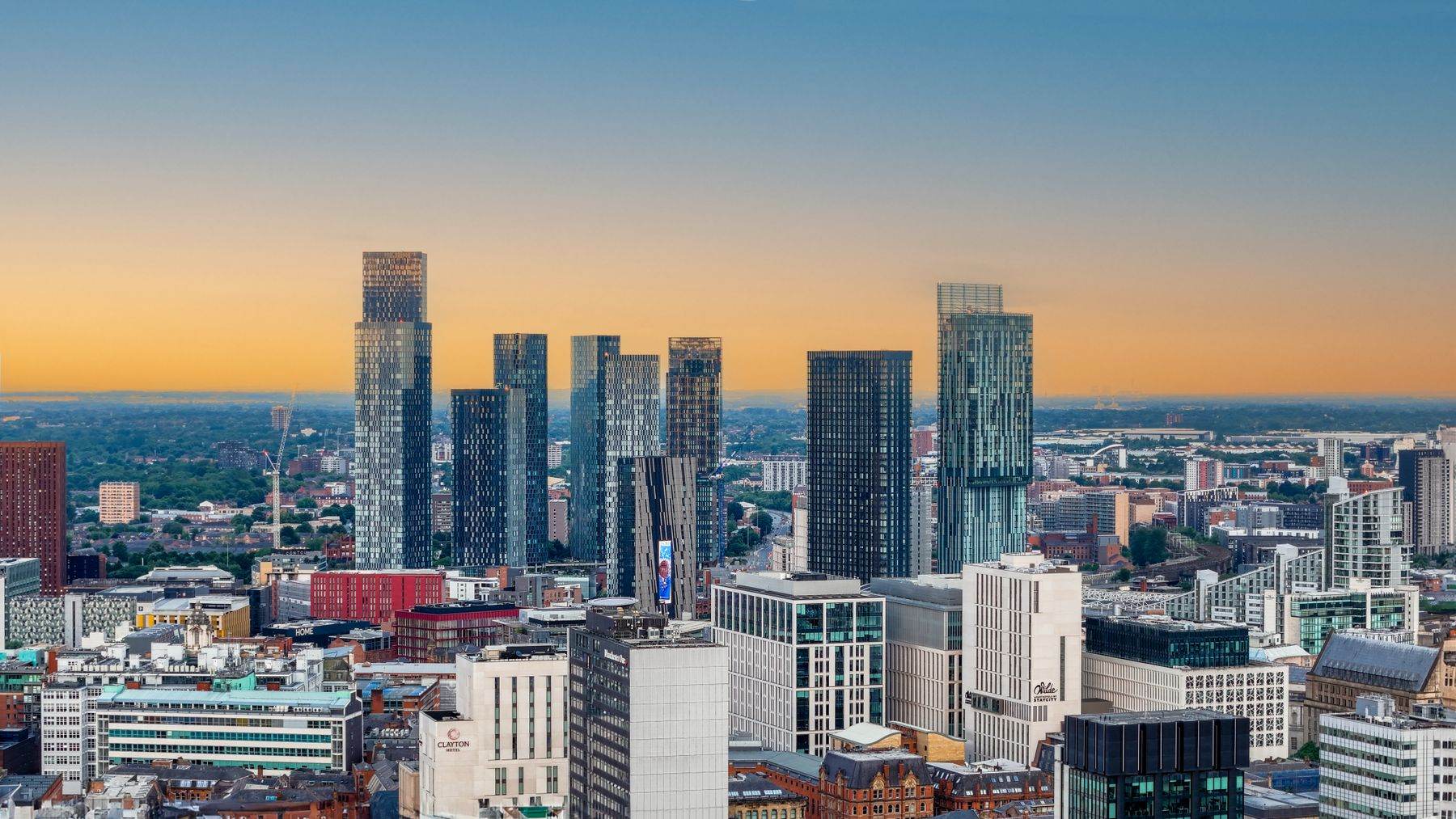 Manchester city-centre skyline at sunrise, the towers lit gold against a clear sky