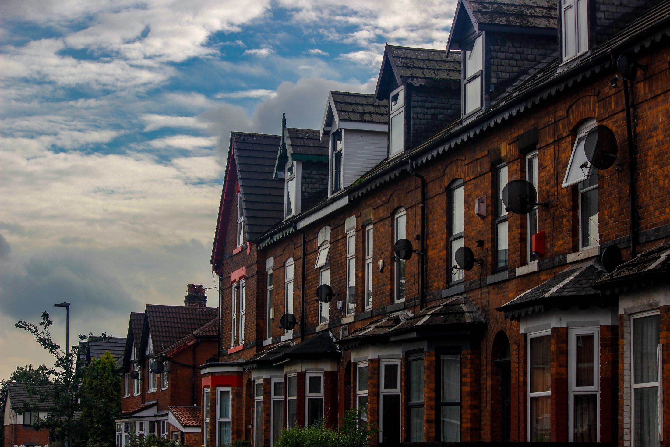 A row of red-brick Victorian terraced houses in a Manchester suburb